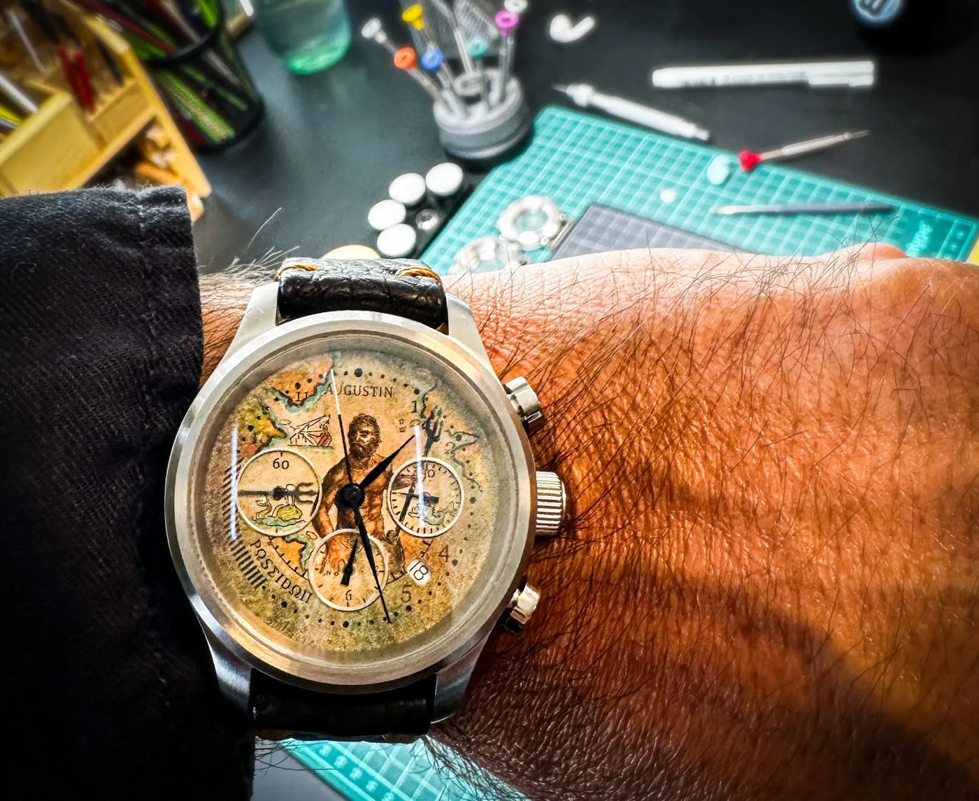 Ceasul Poseidon la încheietură, cu figura pictată peste o hartă veche, în atelier